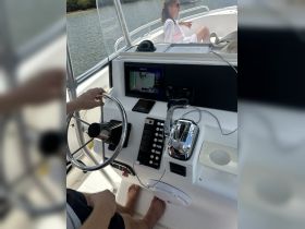 A view of the helm and console inside a boat, featuring a steering wheel and navigation equipment, with a passenger relaxing in the background.