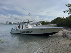 A couple enjoys a moment on the 'GET REEL' fishing boat, anchored near the shoreline, perfect for a day of fishing and relaxation.