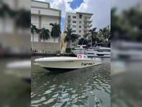 A sleek speedboat named 'GET REEL' docked in calm waters, surrounded by palm trees and residential buildings, perfect for fishing or leisure outings.