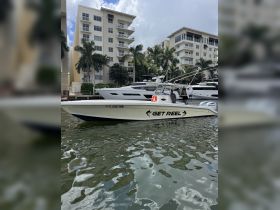 A sleek speedboat named 'GET REEL' docked in a marina, surrounded by luxury yachts and palm trees, showcasing the perfect setting for a day on the water.