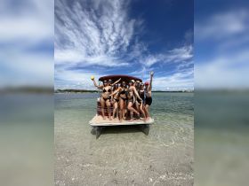 A lively group of friends celebrates on the deck of a pontoon boat at the beach, capturing the essence of summer fun and camaraderie.