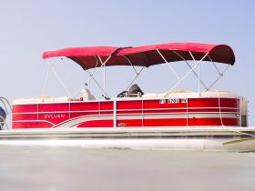 A vibrant red Sylvan pontoon boat docked and ready for a day on the water, showcasing its spacious design and comfortable seating.