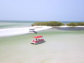 Aerial view of two pontoon boats anchored near a picturesque sandbar, surrounded by clear waters and lush greenery — an ideal setting for a relaxing day on the water.