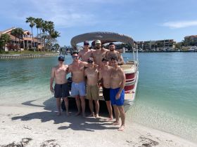 A group of friends enjoys a sunny day at the beach, posing together in front of their pontoon boat — perfect for a fun day on the water.
