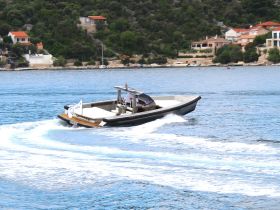 A sleek speedboat navigates through clear waters, showcasing its design and performance against a picturesque coastal backdrop.