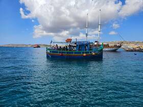 A vibrant fishing boat with guests onboard navigates the clear waters, showcasing a picturesque coastal scene perfect for exploring the beauty of the sea.