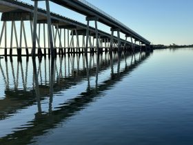 A serene view of a bridge reflected in calm waters, capturing the tranquility of the scene.