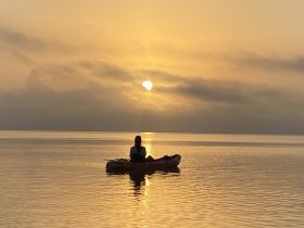 A serene moment captured as a kayaker enjoys a stunning sunset on calm waters, perfect for peaceful reflections and nature appreciation.