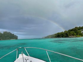 A stunning view from the bow of a boat showcasing a vibrant rainbow over turquoise waters and lush island scenery — a perfect moment for nature lovers.