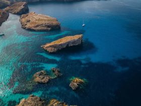 A stunning aerial view of a yacht navigating through crystal-clear waters, surrounded by rocky cliffs and vibrant marine life — an ideal scene for exploring coastal beauty.