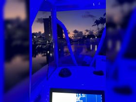 A view of the boat's helm illuminated in blue light, showcasing the dashboard and a serene marina at dusk — perfect for evening cruises.