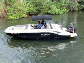 A couple of individuals enjoy a leisurely ride on a sleek boat, showcasing the perfect day on the water surrounded by lush greenery.