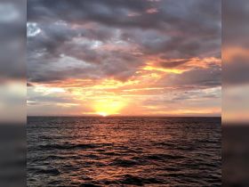 A breathtaking sunset over the ocean, showcasing vibrant colors and serene waters — perfect for capturing the beauty of nature during a boat trip.