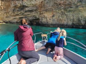 A family enjoys a scenic moment on a boat, with children peering over the edge to explore the crystal-clear waters — a perfect adventure for young explorers.