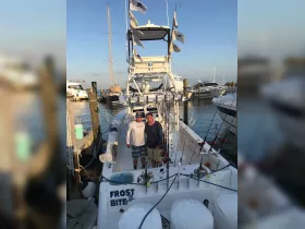 Two friends pose on the deck of the 'Frost Bite' fishing boat at the dock, ready for an exciting day of fishing adventures.