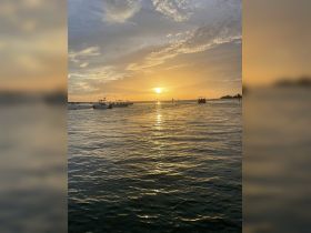 A picturesque sunset over the water with boats silhouetted against the vibrant sky, creating a serene atmosphere perfect for evening cruises.