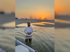 A man enjoys fishing in shallow waters at sunset, creating a serene backdrop for a perfect evening on the beach.