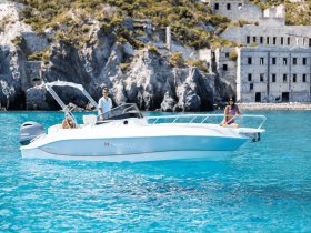 A couple enjoys a sunny day on a Marinello boat, surrounded by stunning turquoise waters and rocky cliffs, perfect for a memorable boating adventure.