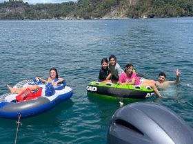 A lively group enjoys a fun day on the water, relaxing on inflatable tubes and swimming in the clear blue lake — perfect for family outings and summer adventures.