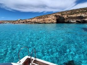 A stunning view of a vibrant turquoise bay with people enjoying the beach and rocky coastline, perfect for a day of relaxation and adventure.
