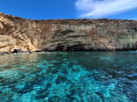 A stunning view of a rocky coastline with a cave, surrounded by crystal-clear turquoise waters — a perfect spot for exploration and adventure.