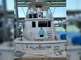 A man stands on the deck of the 'All About Me' boat, showcasing the spacious seating area and helm, perfect for relaxing and enjoying time on the water in Lake Charles.