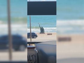 An unclear view of a statue near the beach, with a vehicle parked nearby. The image lacks focus and clarity.