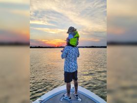 A parent and child enjoy a beautiful sunset on the water, creating cherished family memories aboard their boat.
