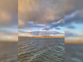 A stunning view of a rainbow arching over a serene coastline, capturing the beauty of nature during a boating trip.