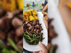 A delicious spread of grilled steak, corn, and asparagus served on a boat, with guests enjoying the water in the background — perfect for a fun day on the water.