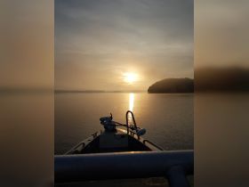 A serene view from the front of a boat at sunset, showcasing the calm waters and distant shoreline — perfect for peaceful evening cruises.