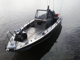 A sleek fishing boat anchored in calm waters, showcasing its spacious deck and fishing gear — perfect for a day on the lake.