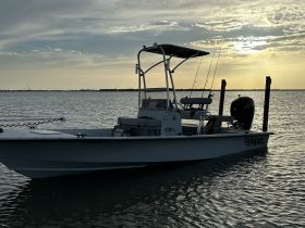 A side view of a fishing boat anchored in calm waters under a beautiful sunset, showcasing its sleek design and fishing gear.