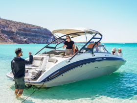 A lively group enjoys a day on the water, interacting on a boat anchored in crystal-clear turquoise waters — perfect for beach outings and celebrations.