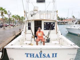 A cheerful individual gives a thumbs up while seated on the deck of the THAISA II, ready for a fishing adventure at the dock.