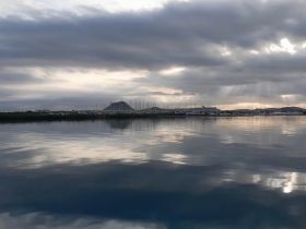 A serene view of a harbor at sunset, with reflections on the water and a backdrop of distant hills — perfect for capturing the tranquility of coastal landscapes.