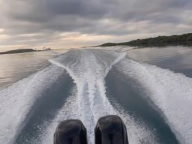 A dynamic view from the back of a boat, showcasing the wake as it glides through calm waters under a cloudy sky — perfect for adventure seekers and boating enthusiasts.