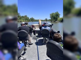 A group enjoys a day on the river aboard a fishing boat, with a dog standing at the bow, capturing the essence of outdoor adventure and camaraderie.