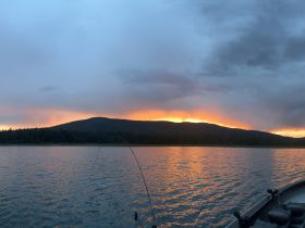 A serene sunset view over a tranquil lake, with a fishing rod in the foreground, creating a perfect backdrop for a peaceful fishing experience.