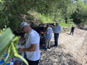A group of friends enjoys a barbecue in a scenic outdoor setting, showcasing camaraderie and culinary fun in nature.