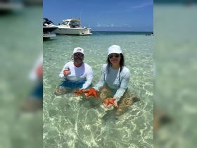 A couple enjoys a close encounter with vibrant starfish while wading in shallow waters, showcasing the beauty of marine life during their beach adventure.