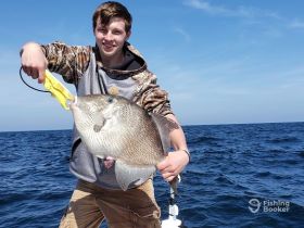 A young angler proudly displays his catch while fishing in the open ocean, showcasing the thrill of a successful fishing trip.