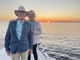 A joyful couple poses on the deck of a boat against a stunning sunset backdrop, capturing a perfect moment of celebration on the water.
