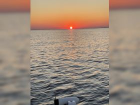 A serene sunset over calm waters, with a glimpse of a boat's equipment in the foreground, creating a picturesque scene perfect for evening cruises.