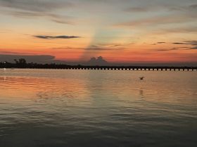 A stunning sunset casts vibrant colors over the water, creating a picturesque reflection — perfect for capturing serene moments on the water.