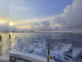A serene sunset view from a fishing boat, showcasing the tranquil waters and fishing rods, perfect for a relaxing day on the water.