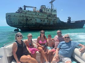 A cheerful family poses on their boat with a shipwreck in the background, capturing a memorable moment on the water — perfect for adventure seekers exploring marine history.