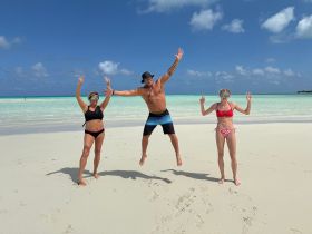 A lively group celebrates on the beach, jumping for joy against a stunning turquoise backdrop — perfect for capturing fun moments during a tropical getaway.