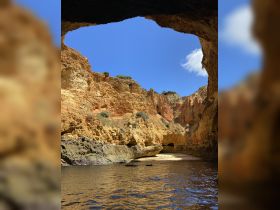 A stunning view of a natural cave along the coastline, showcasing vibrant rock formations and tranquil waters — perfect for exploring scenic destinations by boat.