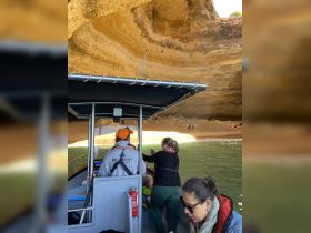 Guests aboard a boat explore a scenic cave, capturing the stunning backdrop of a sandy beach — a perfect adventure for nature lovers.